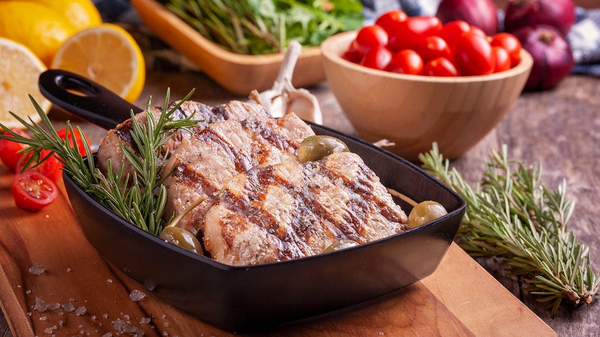 Delicious grilled meat seasoned with rosemary served with fresh vegetables on a wooden board.
